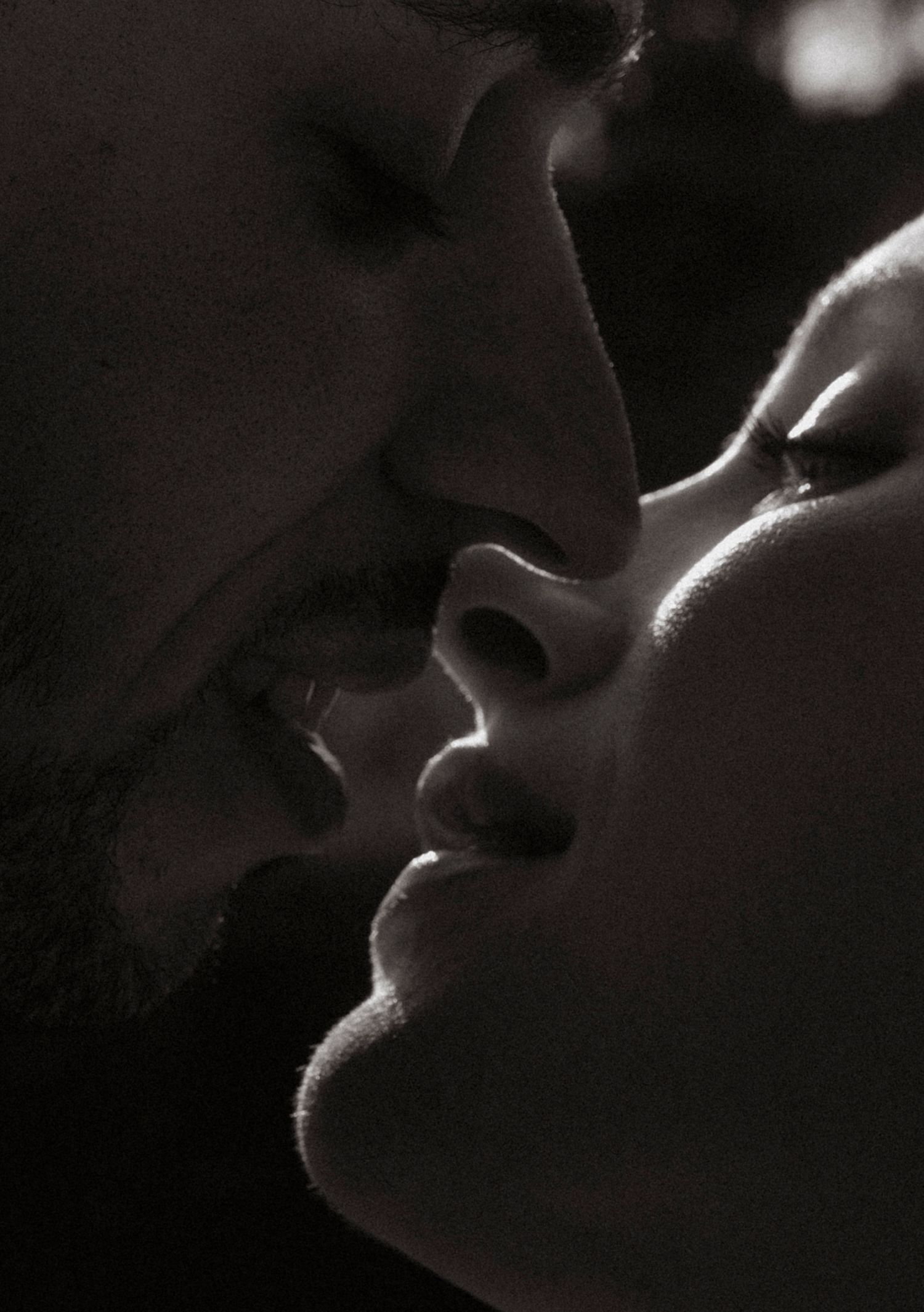 An artistic close-up black and white portrait capturing an intimate moment between two people.