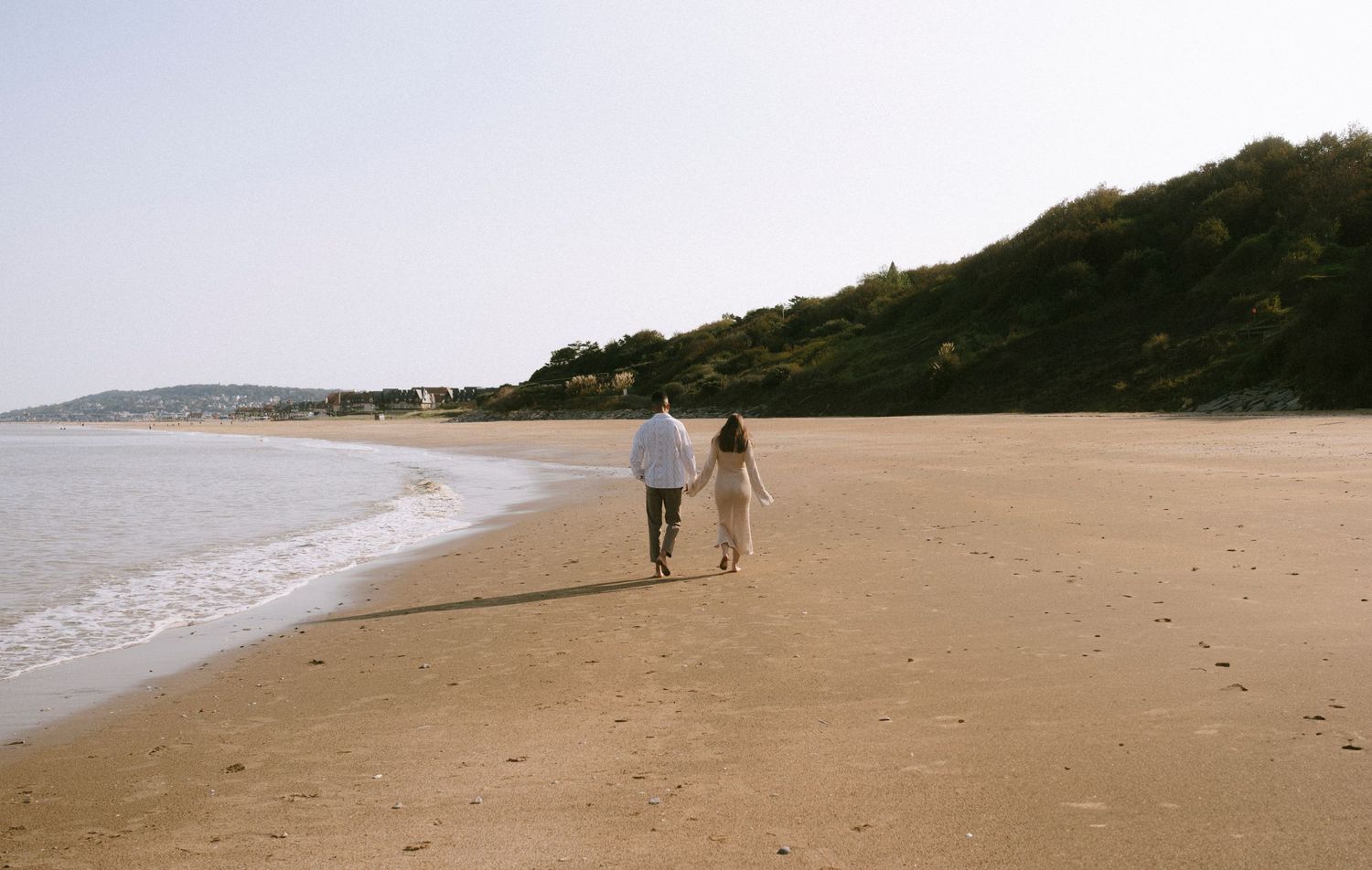 A distant view of two people walking together along an empty beach shoreline.
