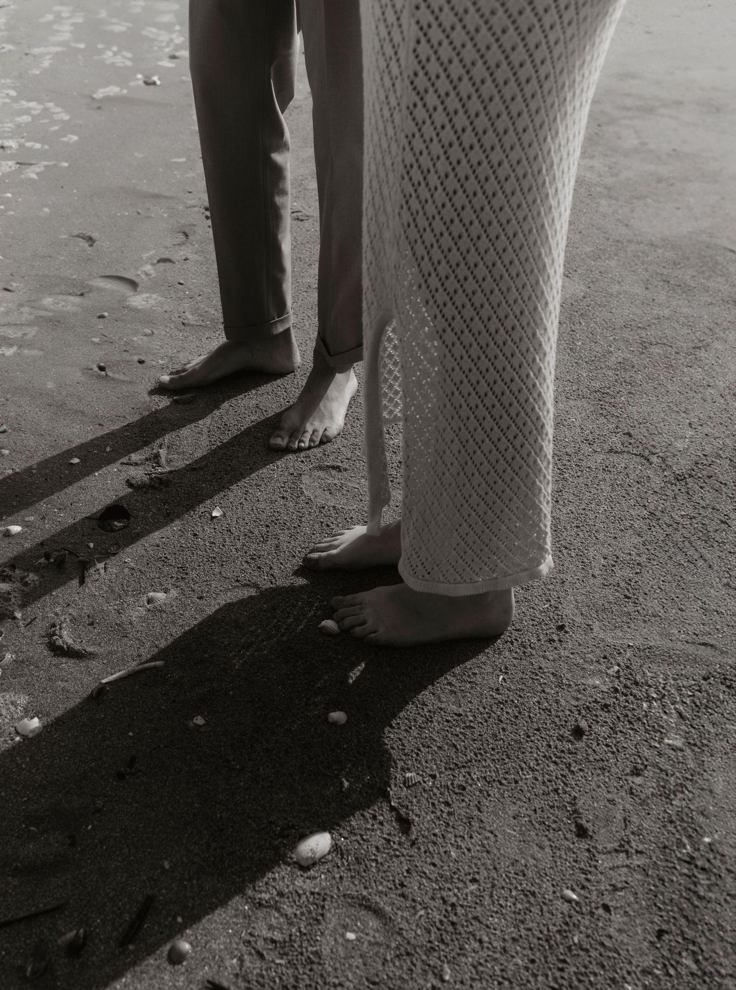 Black and white photo of legs and feet casting dramatic shadows on a textured ground.