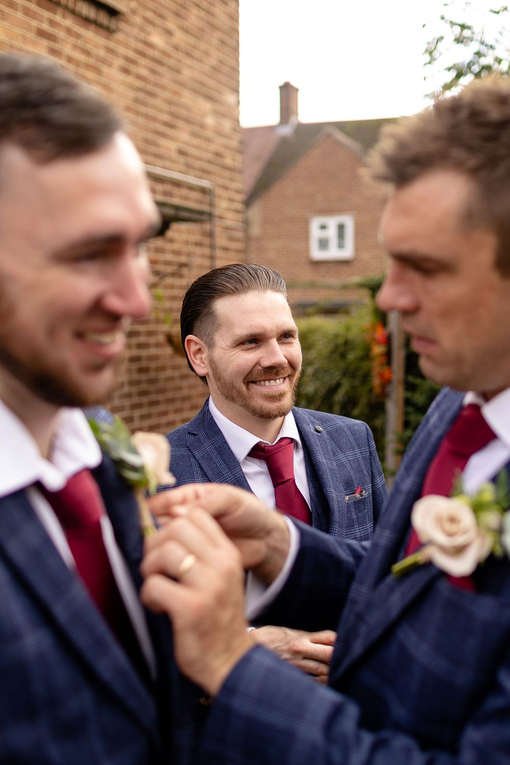 Groomsmen in navy suits and red ties share a lighthearted moment during a wedding celebration.