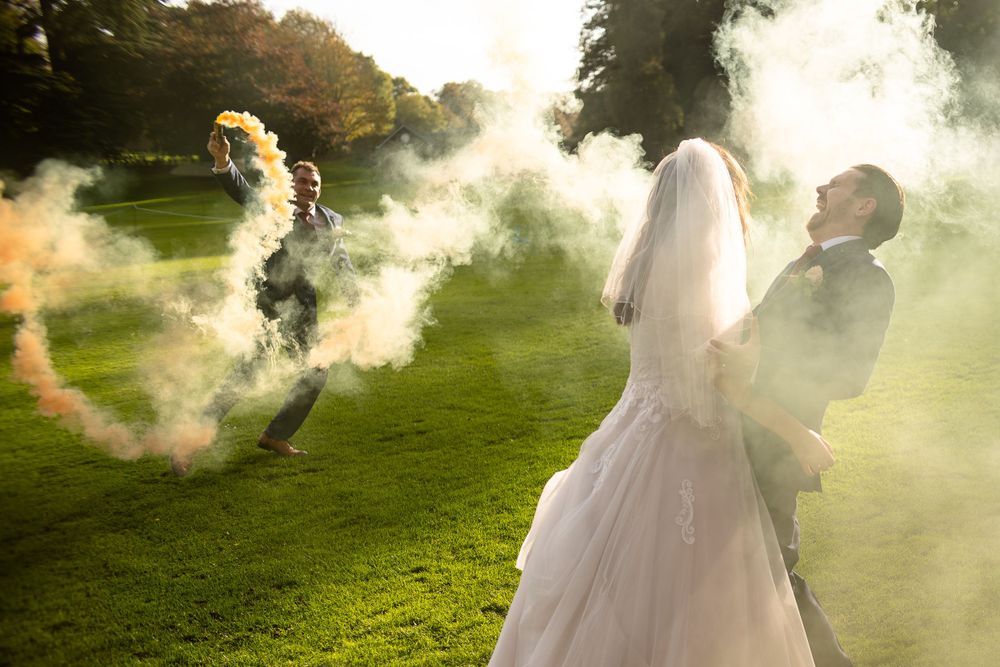 Romantic wedding portrait with smoke effects creating dreamy atmosphere on a sunlit lawn.