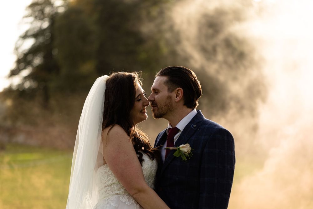 Intimate wedding moment captured in golden smoke at sunset.