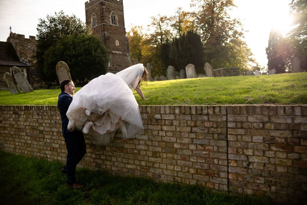 Wedding dress billowing as couple poses by historic church wall.