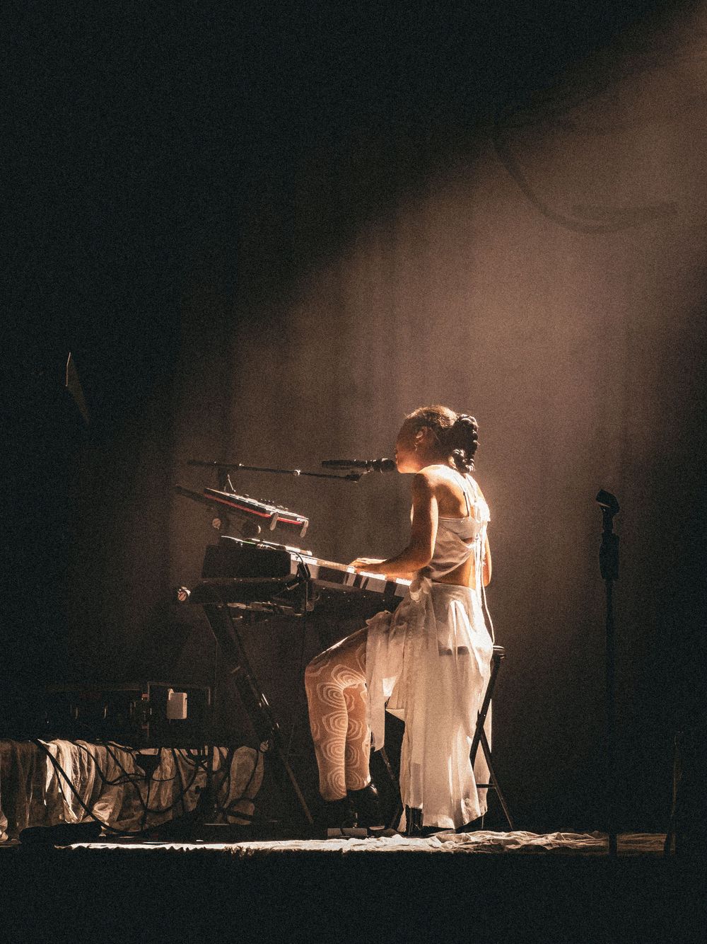 Concert performer in white outfit playing electronic equipment on dimly lit stage.