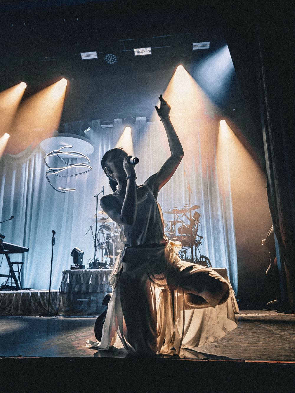 Silhouetted performer raising arm on stage with dramatic backlighting.