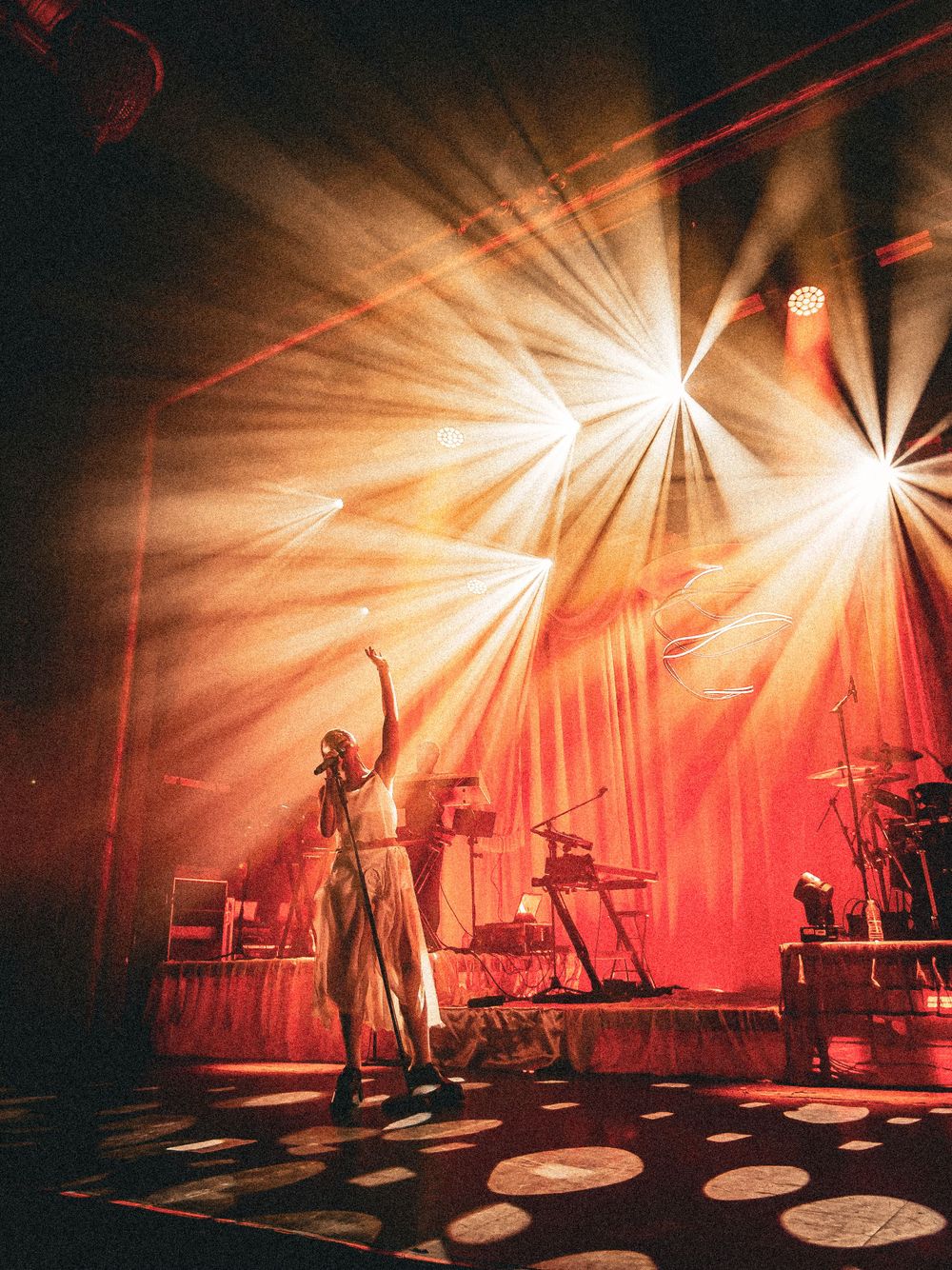 Concert stage with dramatic orange spotlight beams and silhouetted performer.