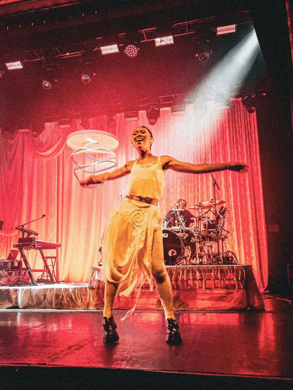 Performer in yellow outfit dancing energetically on stage under bright red and white spotlights.