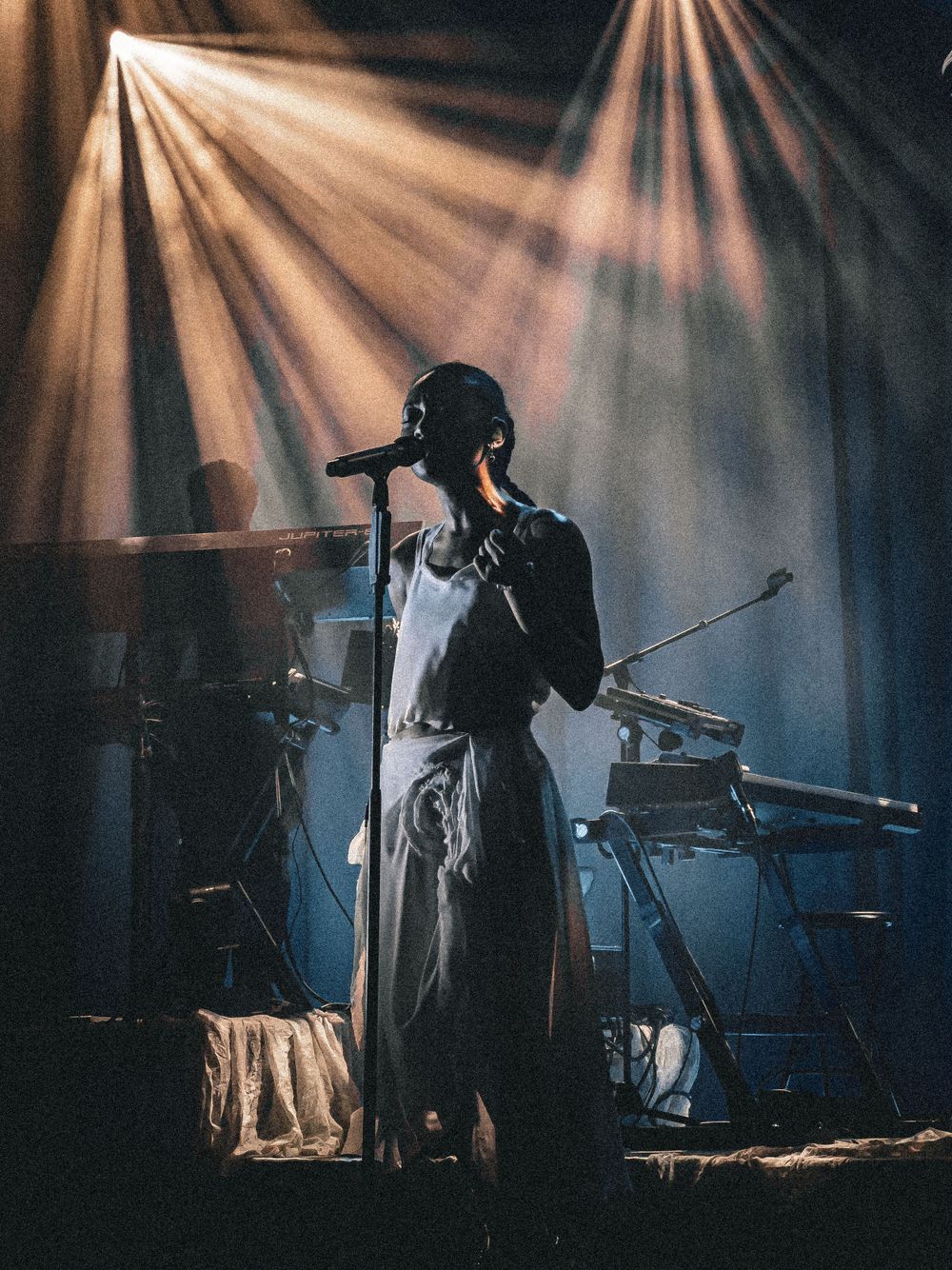 Silhouetted performer singing on stage with dramatic beams of light creating an atmospheric concert scene.