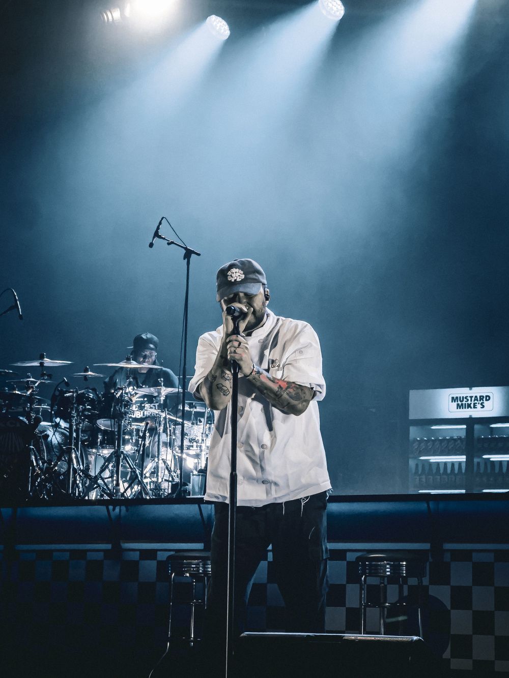 Concert performer on stage with blue spotlight illumination and checkerboard pattern design.