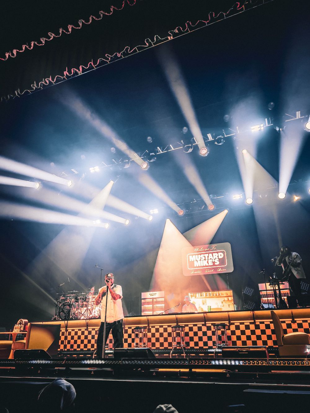 Concert stage with dramatic white spotlights and checkerboard pattern platform design.