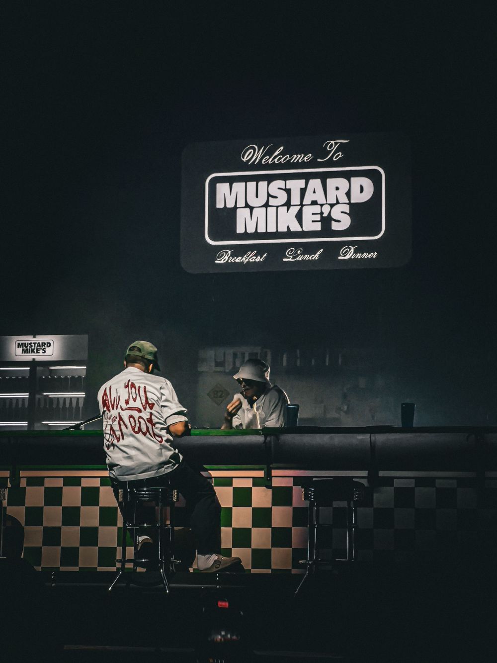 Late night scene at Mustard Mike's diner counter with retro checkerboard design and neon signage.
