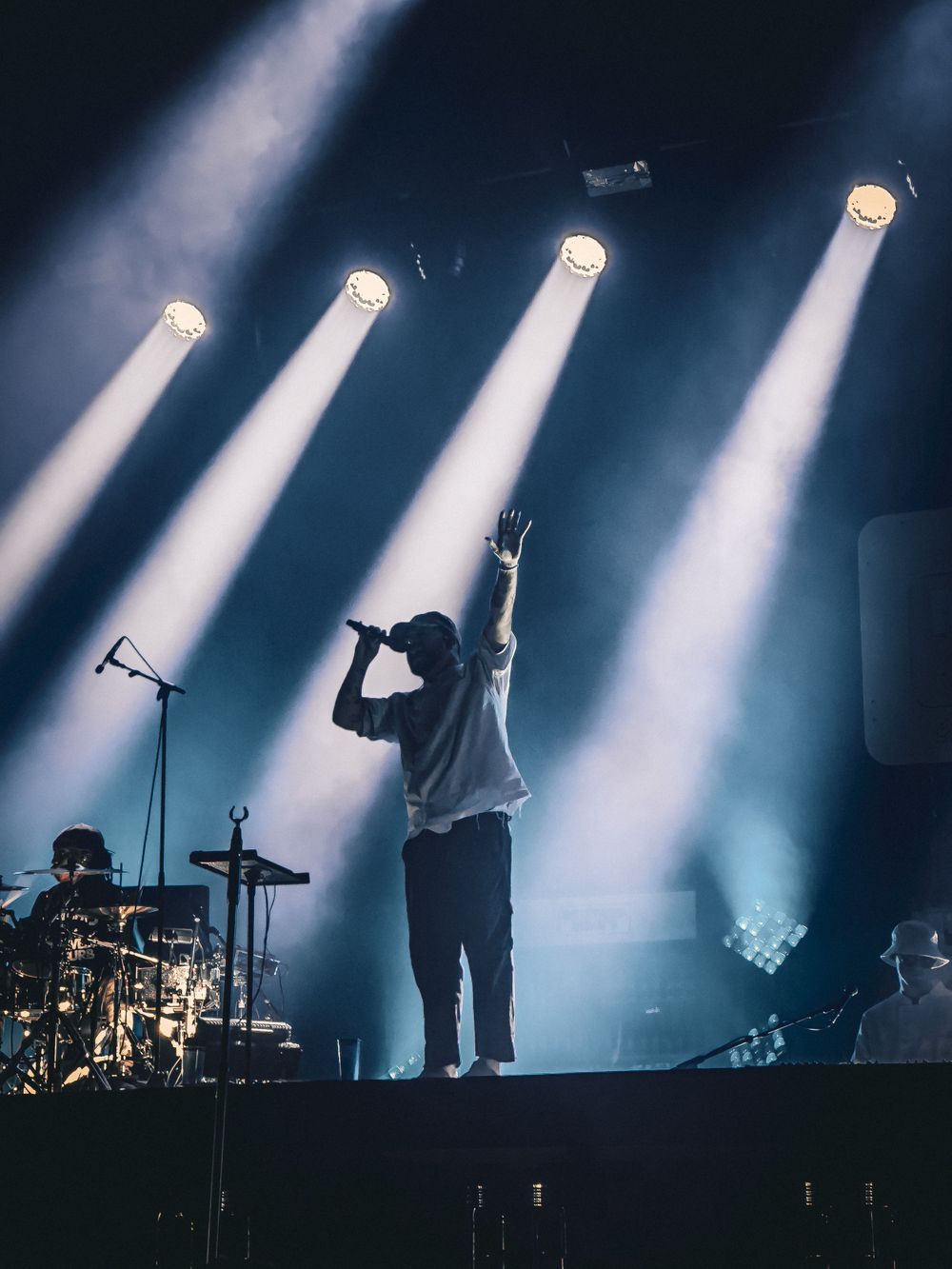 Silhouetted performer on stage with dramatic white spotlight beams cutting through dark atmosphere.
