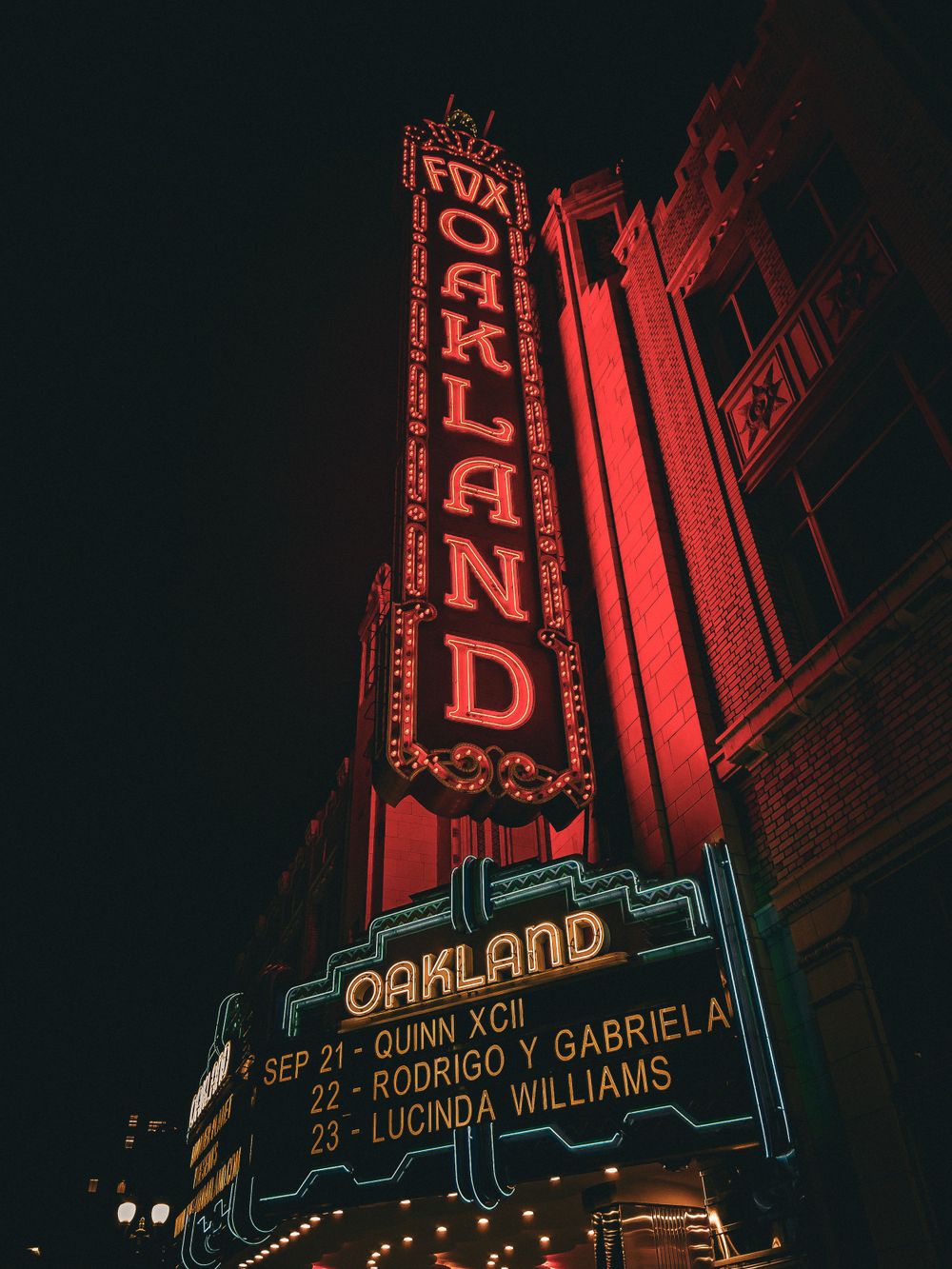 Illuminated red neon Oakland theater marquee sign at night displaying show information.