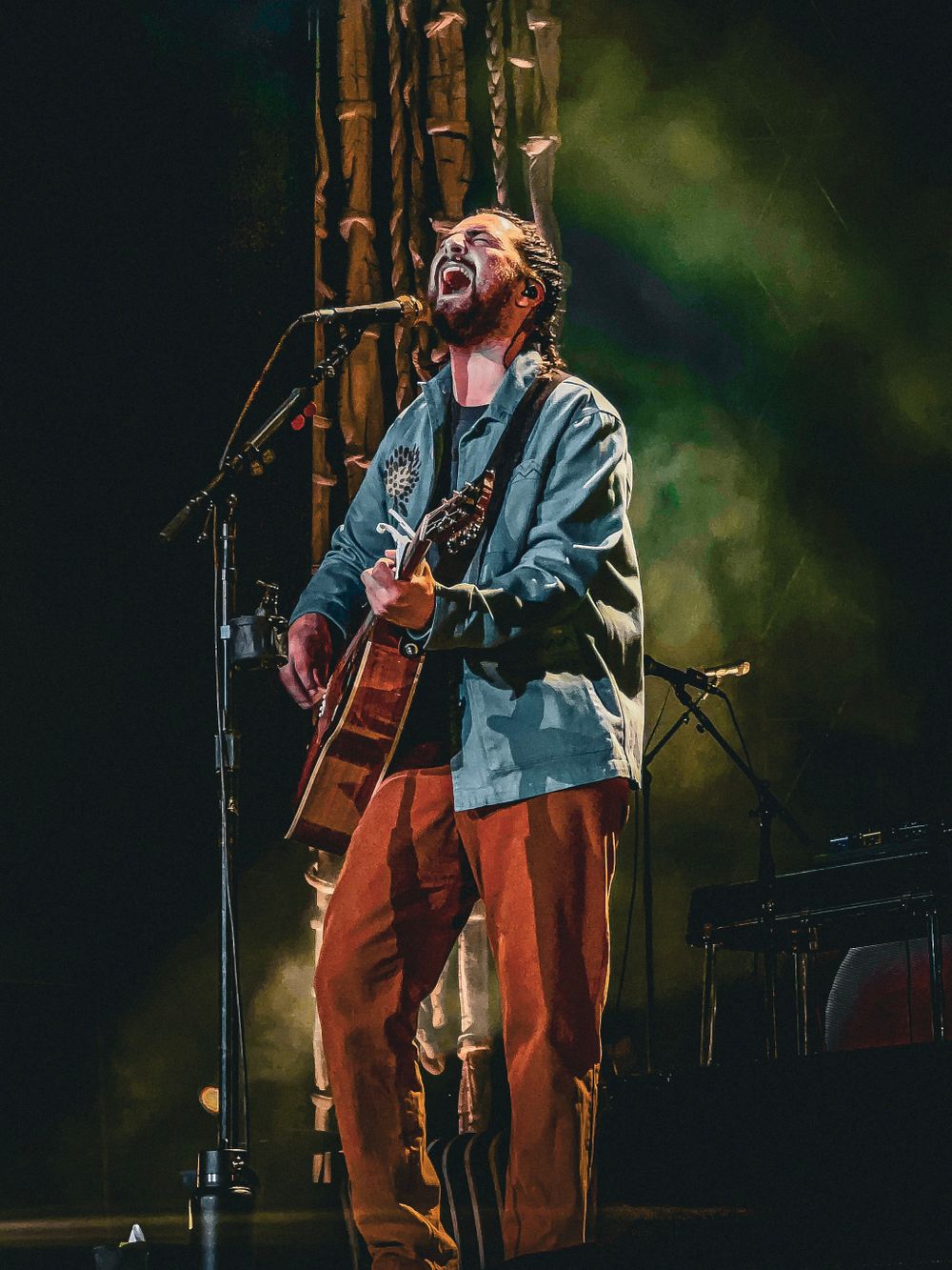 Passionate musician singing and playing acoustic guitar on stage with dramatic lighting effects.