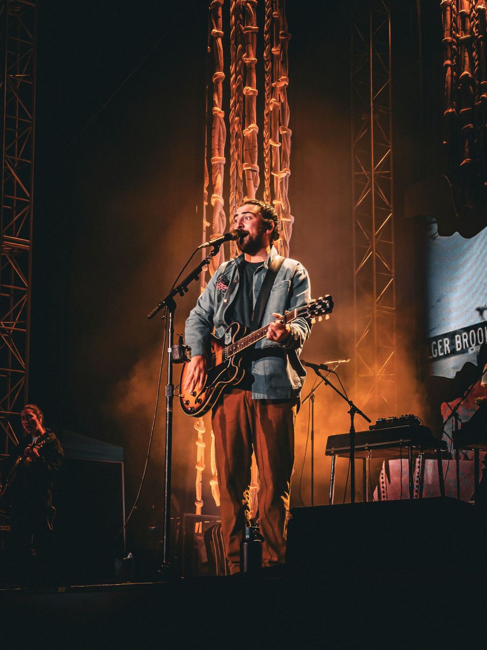 Musician performing with guitar on stage illuminated by warm orange lighting and theatrical effects.