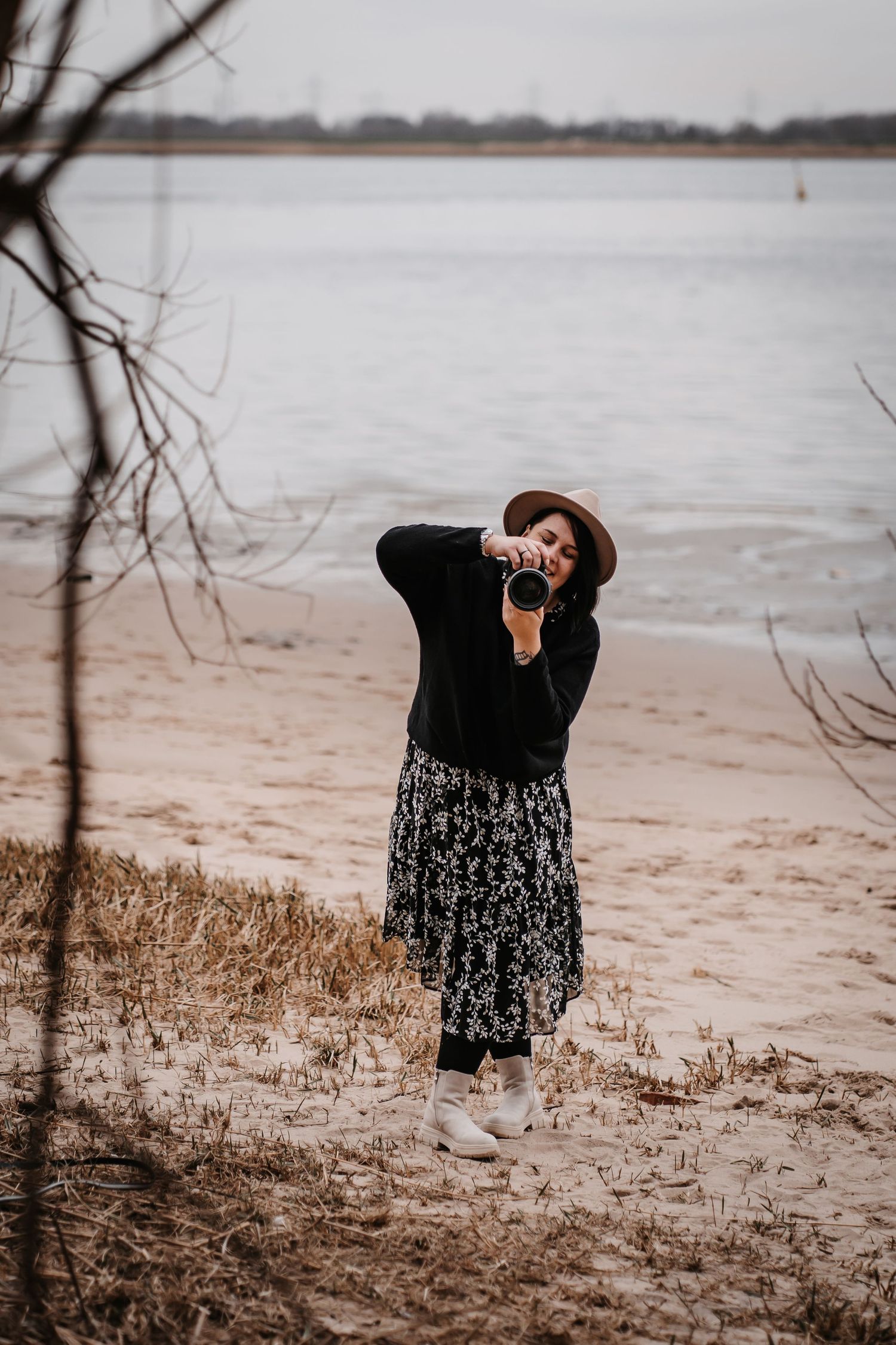 Figure in dark clothing and hat photographs on winter beach landscape.