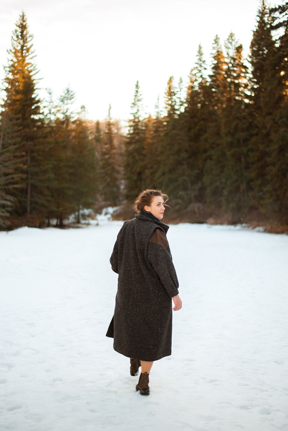 Winter scene with person in dark coat walking through snow-covered forest path.