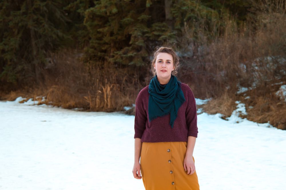 Winter fashion portrait with teal scarf and burgundy sweater against snowy forest backdrop.