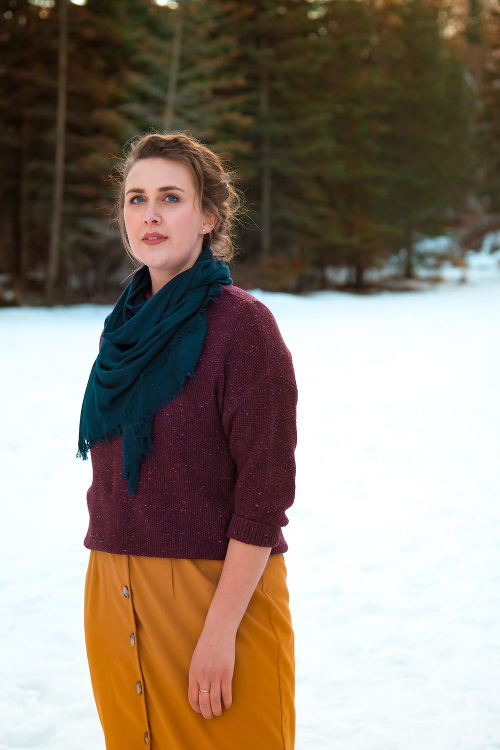 Winter outdoor portrait featuring burgundy sweater and teal scarf against snowy landscape.