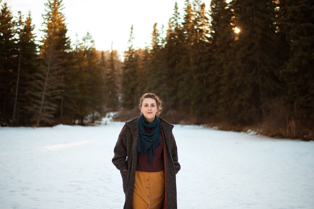 Winter portrait featuring person in layered outfit against snow and evergreen forest background.