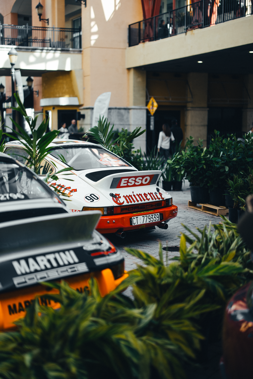 Classic Porsche race cars with Esso and Martini liveries parked among tropical plants at an upscale venue.
