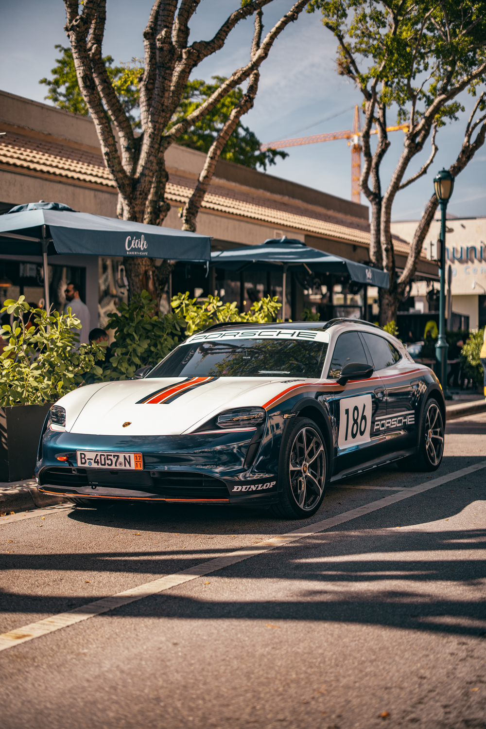 A black and white Porsche Taycan race car with racing stripes parked outside a cafe with green outdoor umbrellas.