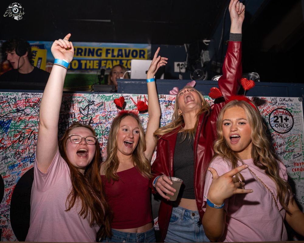 Party goers enjoying themselves at a nightclub with hands raised and celebrating under colorful lighting.