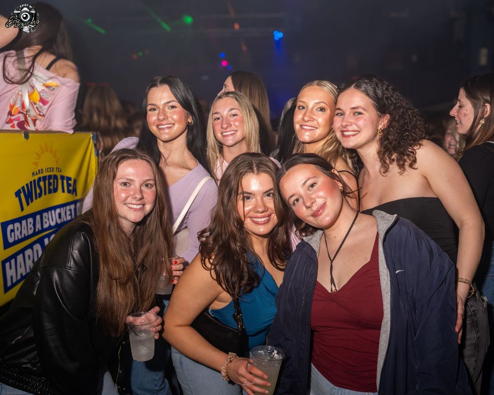 A group of friends enjoying a night out at a club with colorful lighting and party atmosphere in the background.