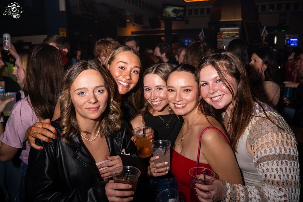 A group of people enjoying drinks and smiling together at a dimly lit bar or nightclub.
