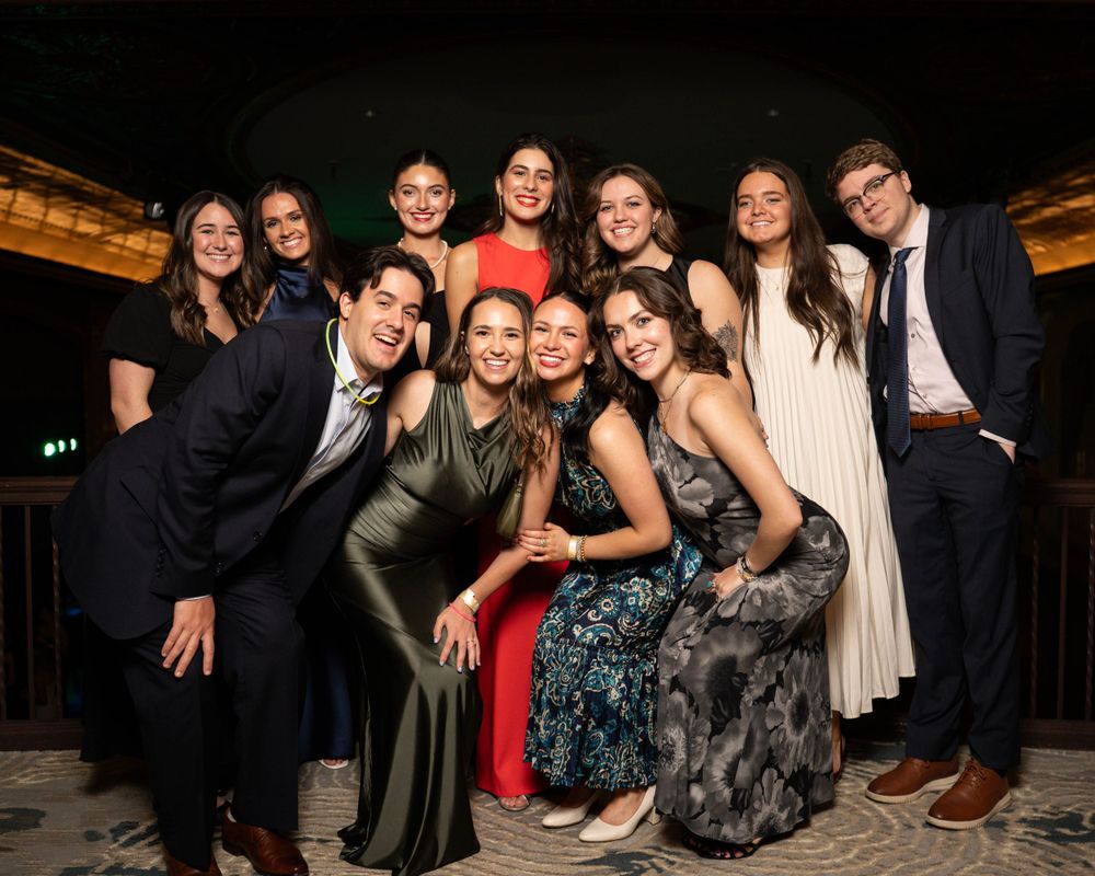 A group in formal evening attire poses together at an elegant event venue with warm lighting.