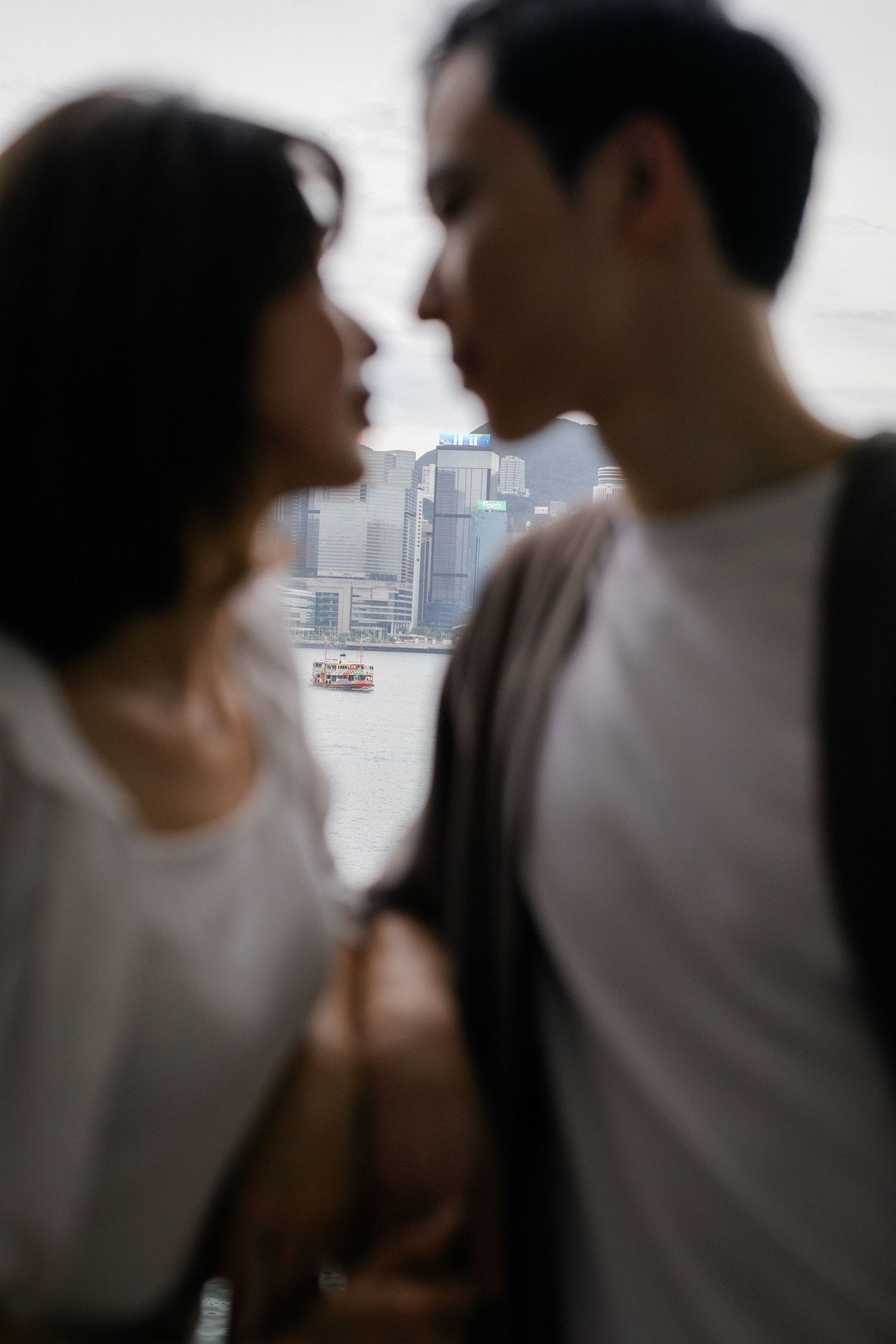 Blurred close-up of Asian couple about to kiss with Hong Kong harbour cityscape visible behind them.