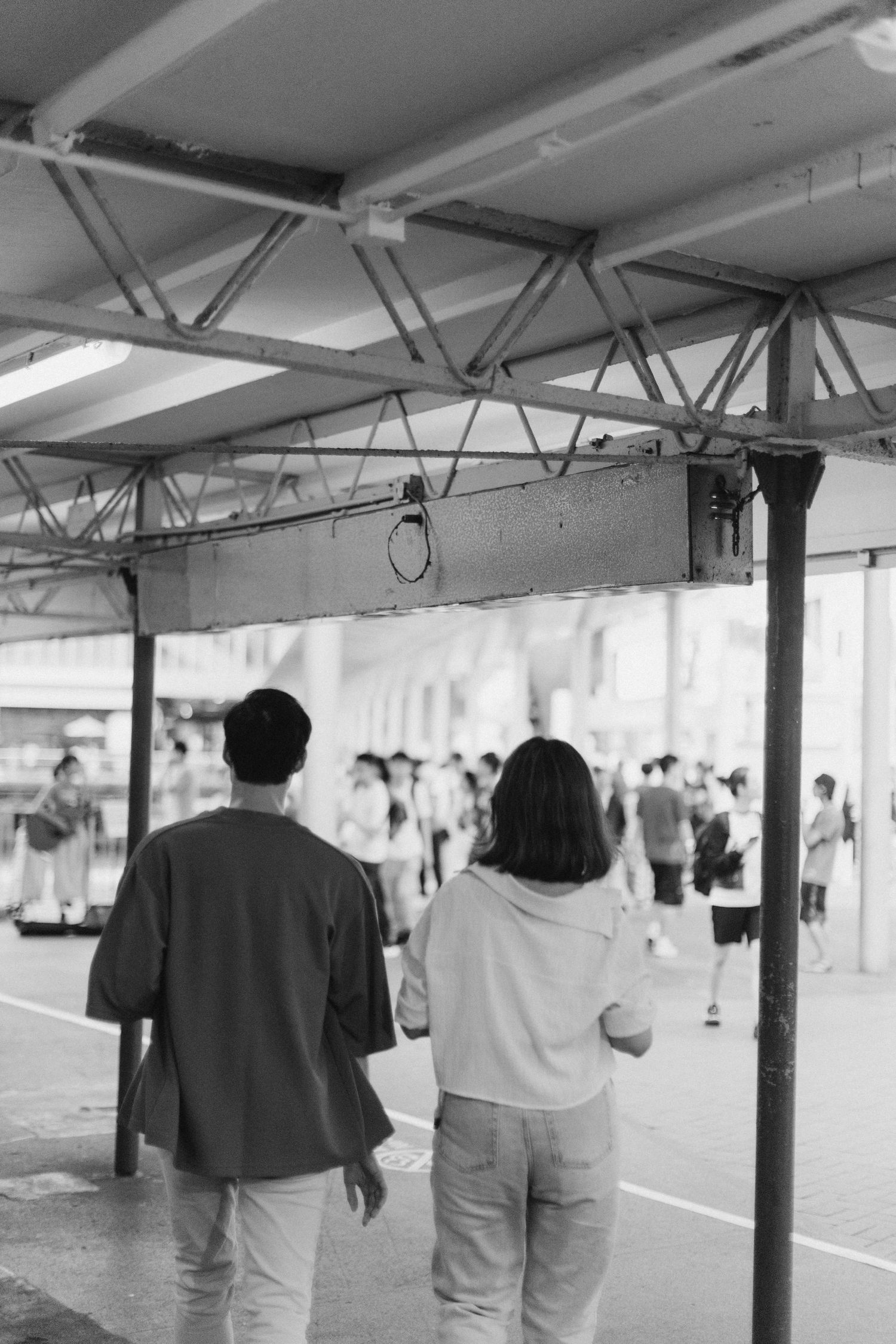 Black and white rear view of a young couple walking together under a covered transit shelter.