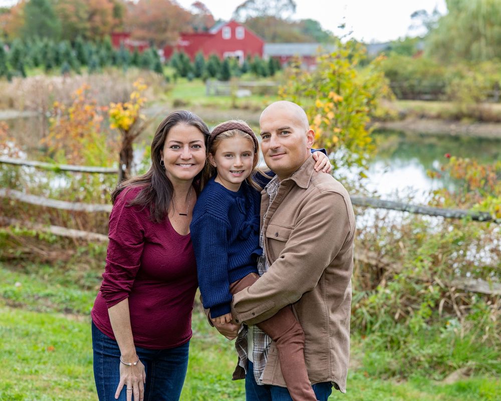 A family wearing burgundy and blue sweaters embraces while posing for their family photography session at Mistletoe Tree Farm in Stow, MA