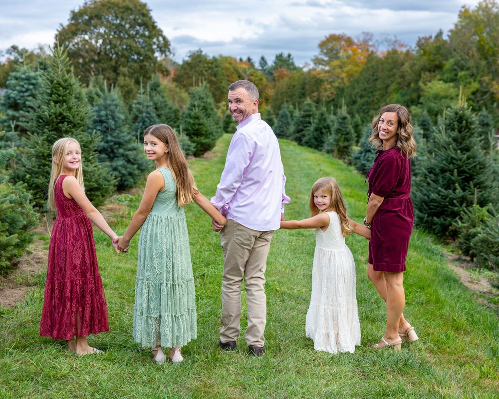 A family in coordinated burgundy, mint green & white outfits walks through Christmas tree farm during their family photo session in Stow, MA