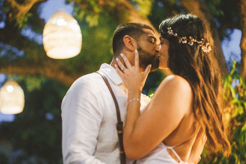 An intimate wedding moment captured at sunset with hanging lanterns in the background.