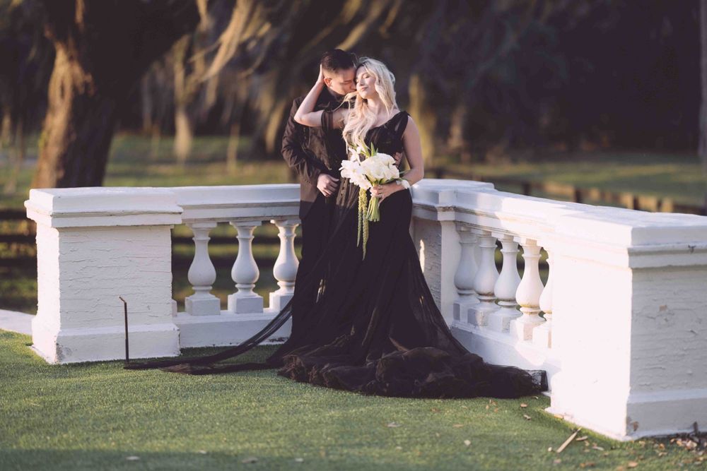 A dramatic portrait of someone in a flowing black dress seated on white stone balustrade.