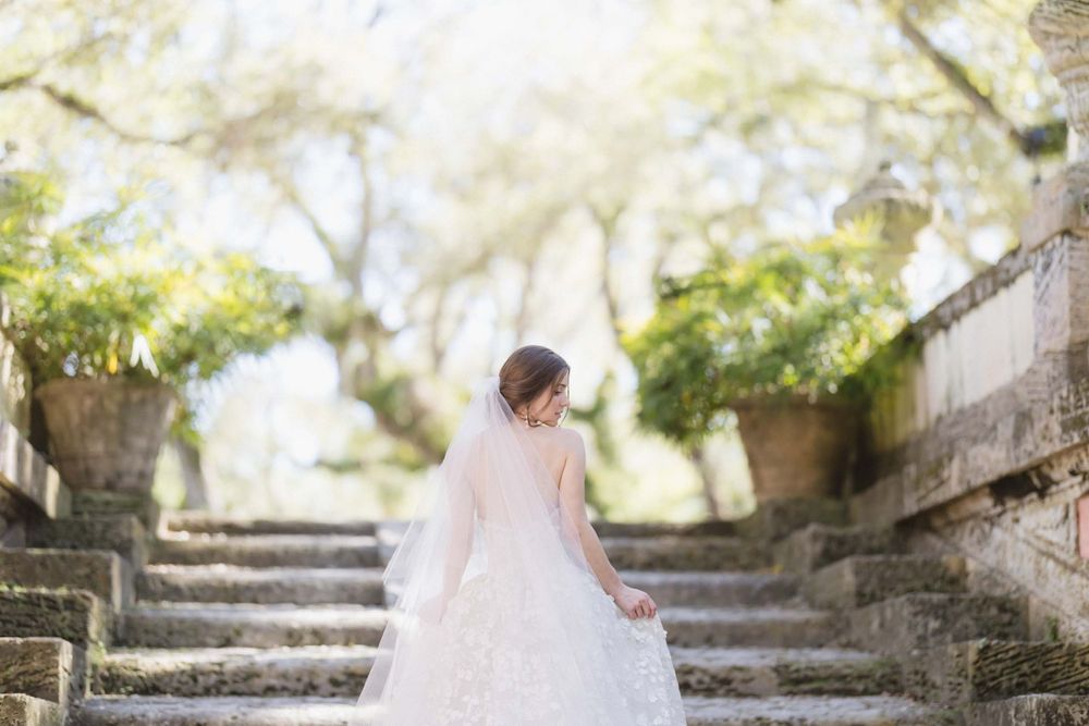 A bride in a flowing white gown poses on stone steps surrounded by dreamy natural light.
