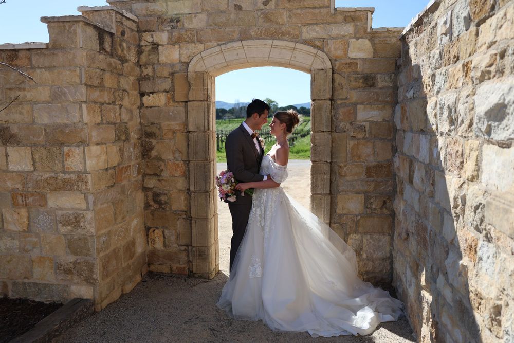 A wedding couple stands in a stone archway during their romantic outdoor ceremony.