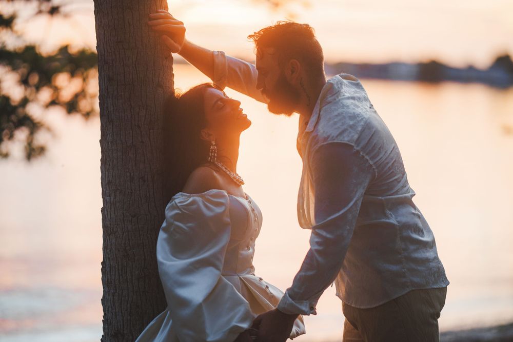 Silhouetted couple shares romantic moment at sunset by tree.