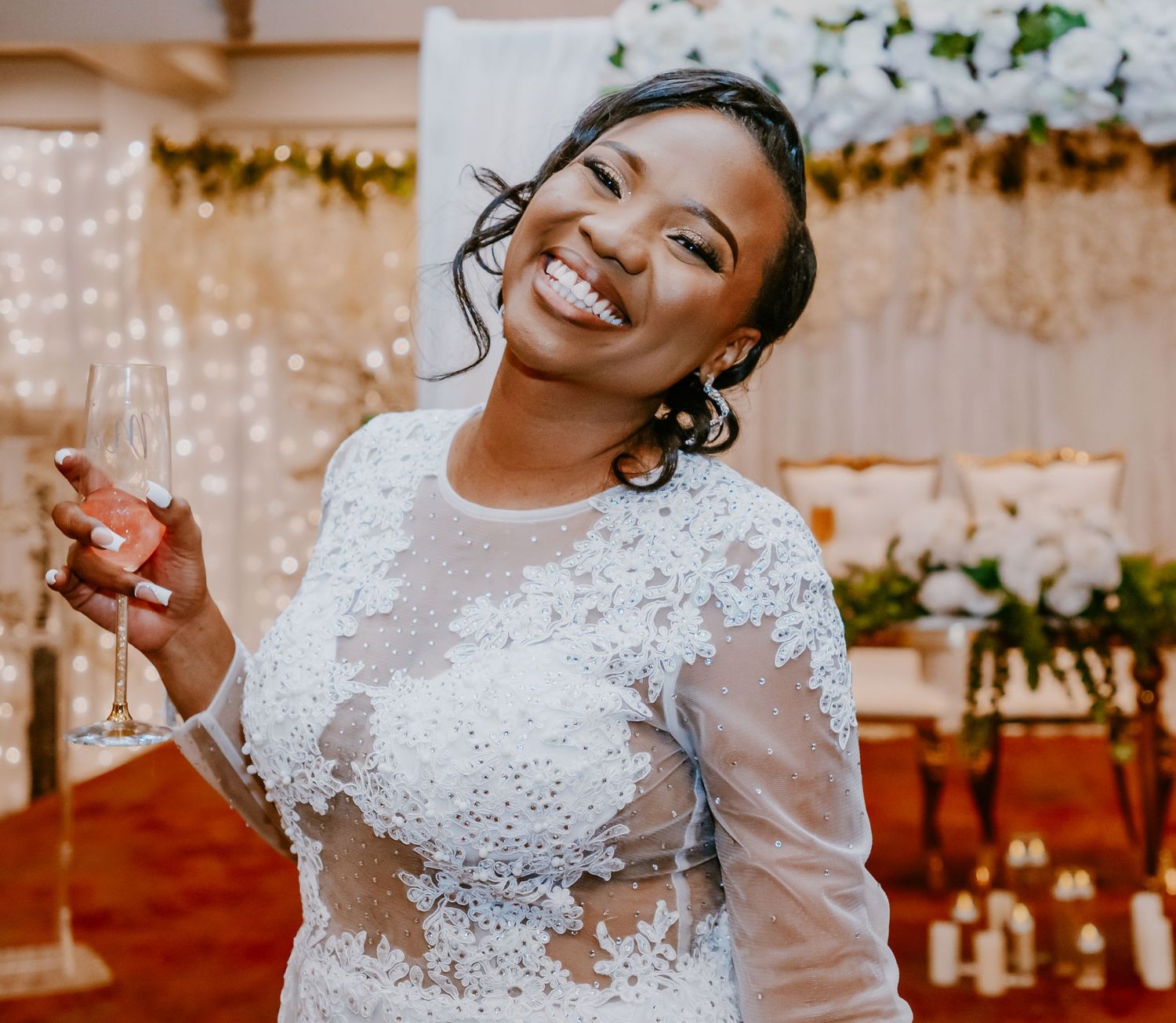 Joyful bride in lace wedding dress holding champagne glass at reception.