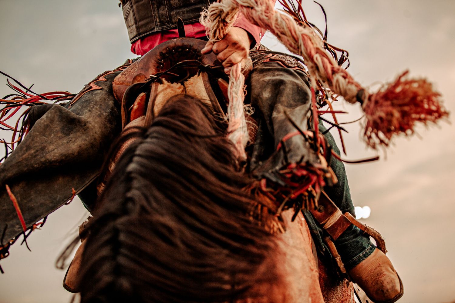 Close-up of rodeo rider equipment with decorative red tassels against cloudy sky.