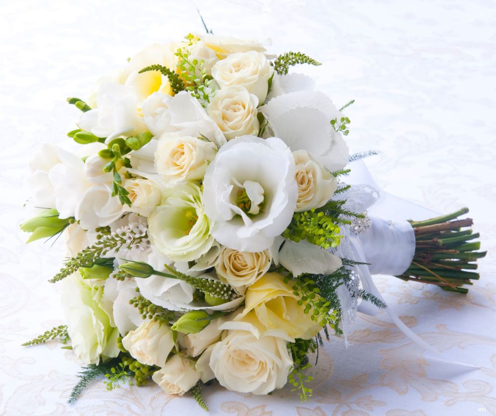 A delicate bridal bouquet of white roses, calla lilies and yellow accents tied together with white ribbon.