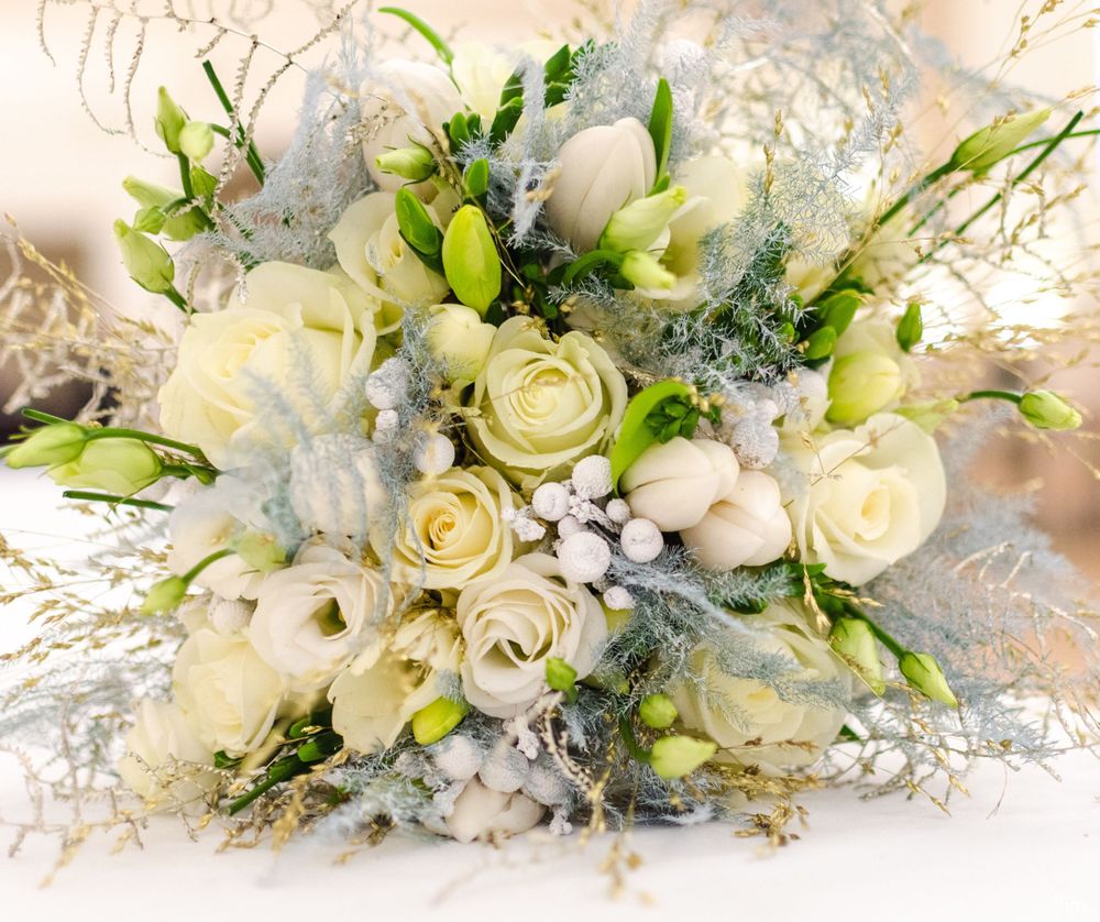A winter white bridal bouquet with cream roses, silver accents, and fresh greenery on a light background.
