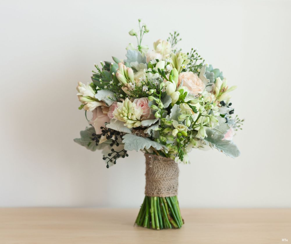 A elegant wedding bouquet with white roses, eucalyptus leaves, and delicate greenery wrapped in burlap ribbon.