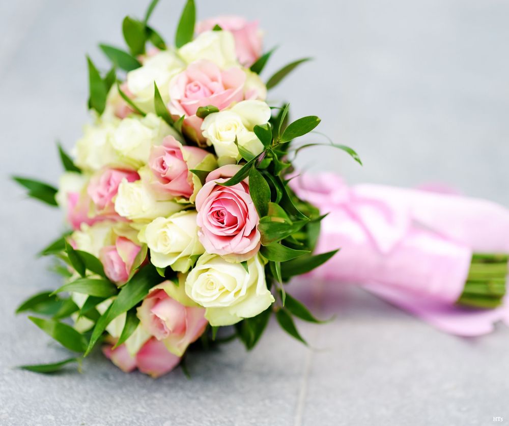 A bridal bouquet of pink and cream roses tied with a pink satin ribbon rests on a light gray surface.