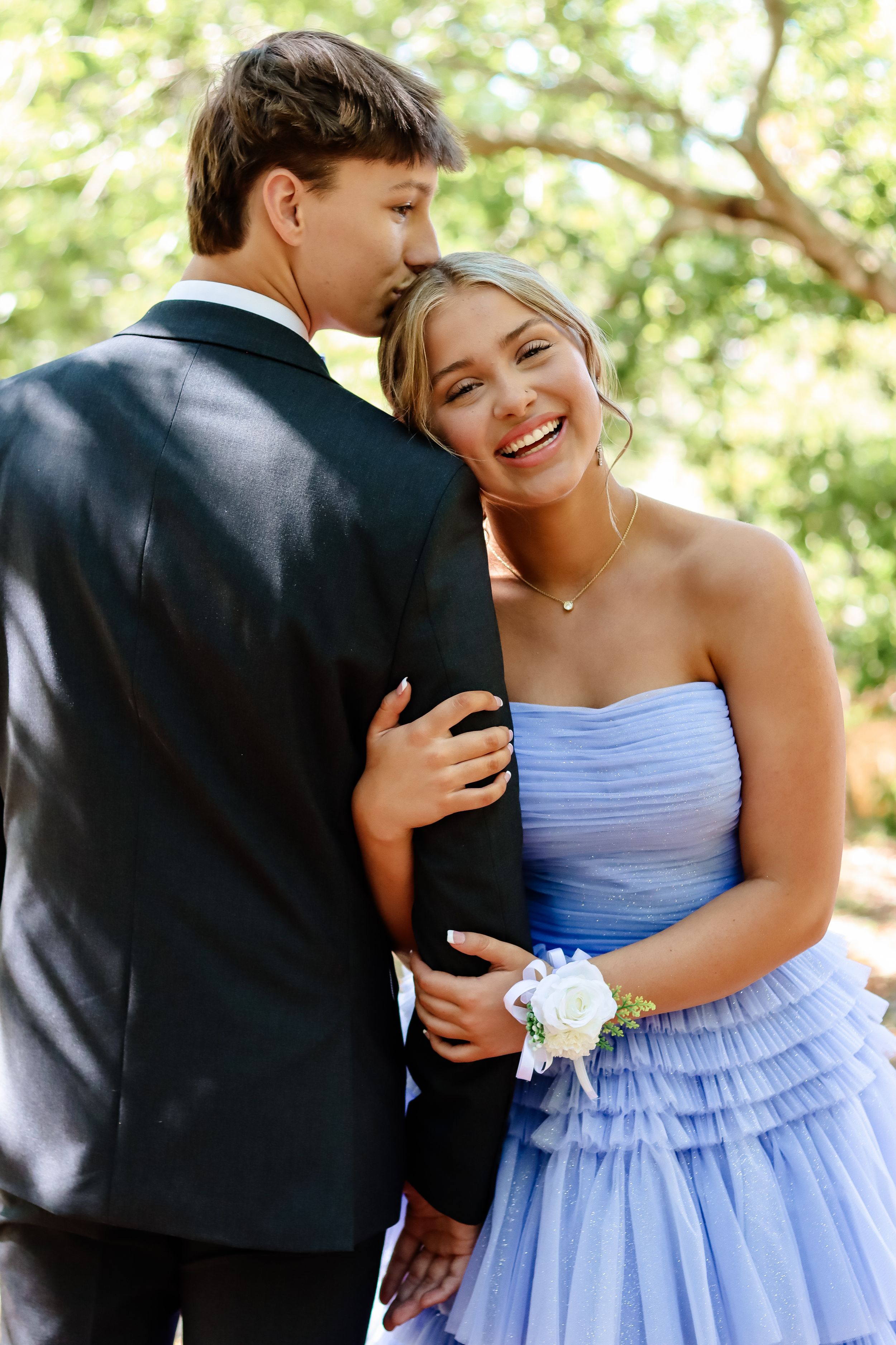 Couple in formal attire shares a moment at outdoor event, with corsage and light purple dress.