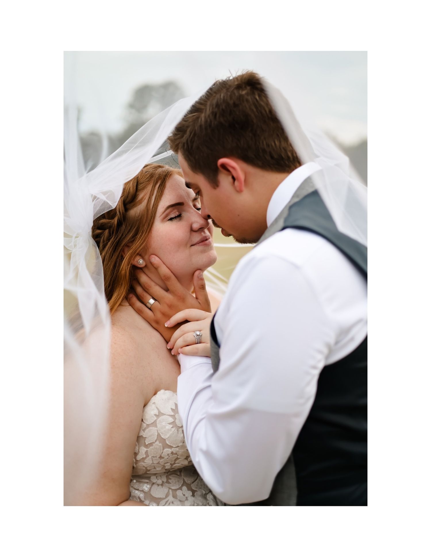 Intimate moment between couple under flowing white veil against light background.