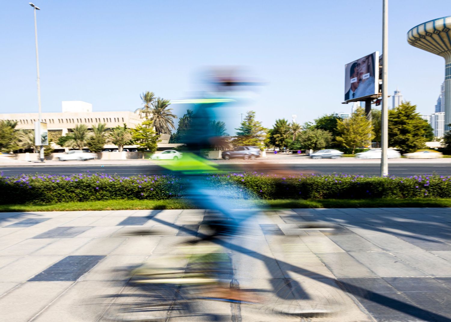 A blurred cyclist rides across a crosswalk in motion with a building and traffic signs in the background.