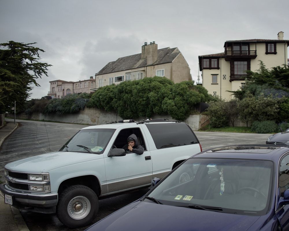 White SUV parked on a hill with residential buildings in the background.