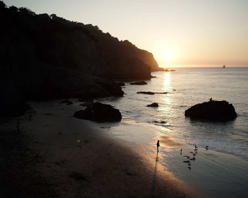 Dramatic sunset over a rocky beach cove with silhouettes on the shore.